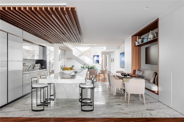 kitchen with a kitchen bar, decorative backsplash, white cabinets, and light stone countertops