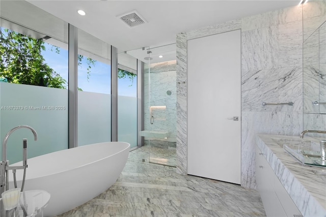 full bath with visible vents, a shower stall, vanity, a soaking tub, and stone wall