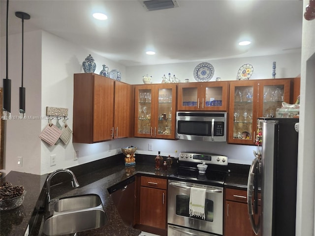 kitchen featuring appliances with stainless steel finishes, dark stone countertops, pendant lighting, and sink