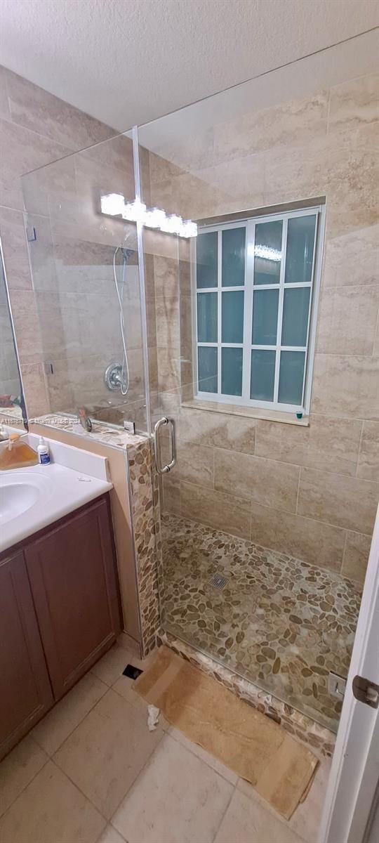 bathroom featuring tile patterned flooring, vanity, a shower with shower door, and a textured ceiling