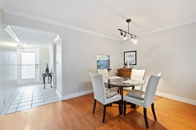 dining space with rail lighting, light hardwood / wood-style floors, a textured ceiling, and ornamental molding