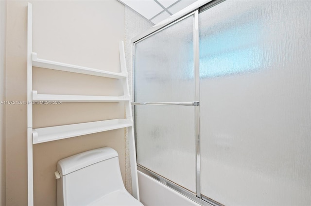 bathroom featuring toilet and bath / shower combo with glass door