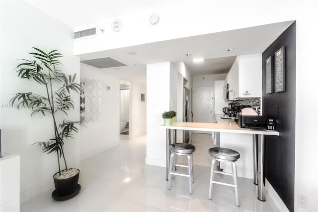 kitchen featuring kitchen peninsula, a breakfast bar, light tile patterned flooring, white cabinets, and tasteful backsplash