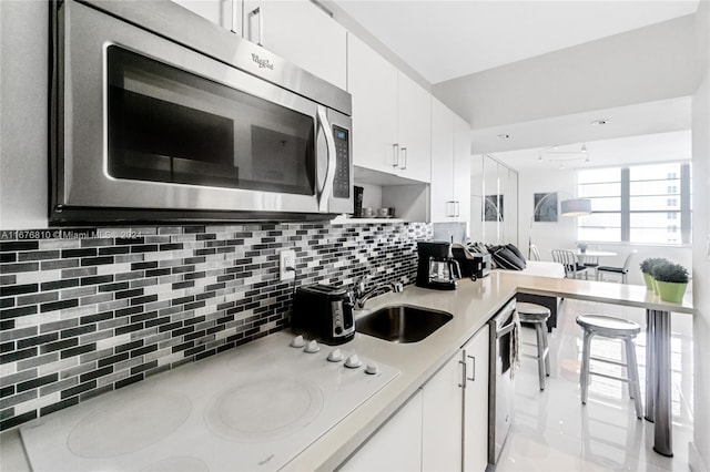 kitchen featuring decorative backsplash, white cabinets, stainless steel appliances, and sink