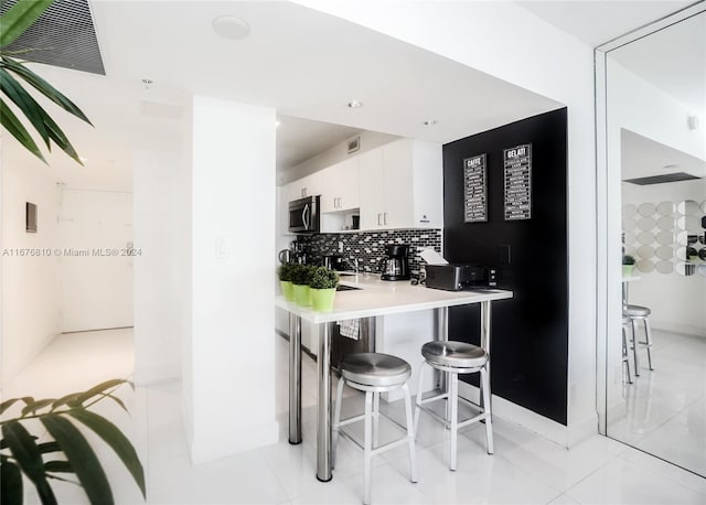 100 Lincoln Rd Unit 1201, Miami Beach, FL 33139 - kitchen featuring stainless steel microwave, white cabinetry, a breakfast bar area, backsplash, and light countertops