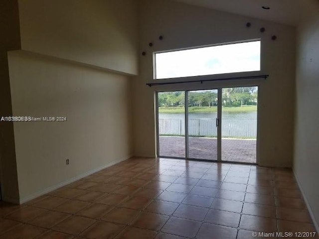 empty room with tile patterned floors, a water view, and high vaulted ceiling