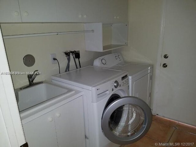 laundry room with dark tile patterned flooring, washer and dryer, and cabinets