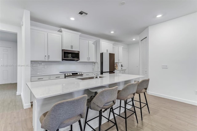 kitchen with a center island with sink, white cabinets, sink, appliances with stainless steel finishes, and a kitchen bar