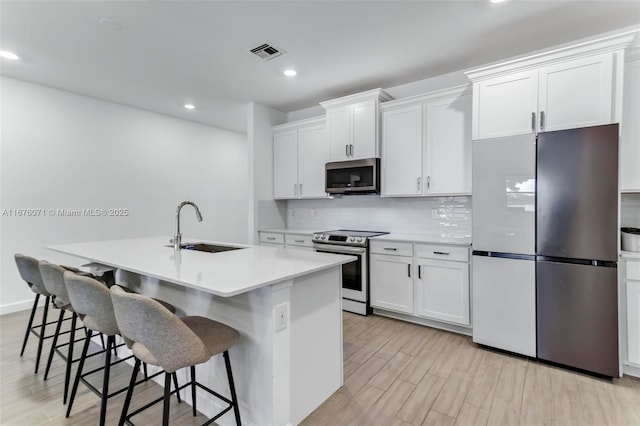 kitchen featuring a kitchen breakfast bar, stainless steel appliances, a kitchen island with sink, sink, and white cabinets