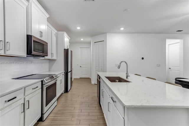 kitchen with light stone countertops, sink, an island with sink, and stainless steel appliances