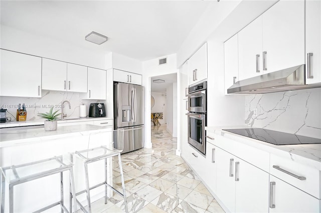 kitchen featuring a breakfast bar area, decorative backsplash, white cabinetry, and stainless steel appliances