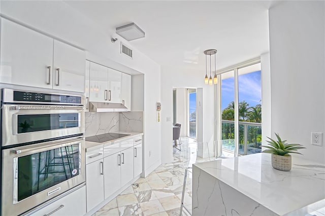 kitchen with stainless steel double oven, white cabinets, decorative light fixtures, and tasteful backsplash