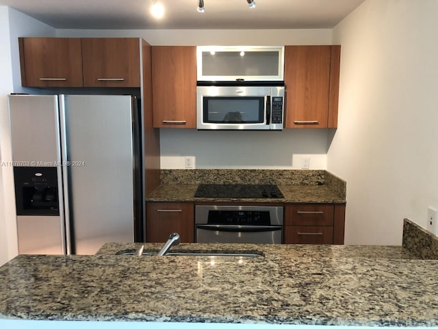 kitchen featuring sink, stainless steel appliances, dark stone counters, and kitchen peninsula