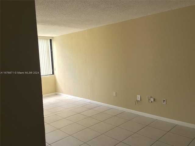 spare room featuring light tile patterned floors, baseboards, and a textured ceiling