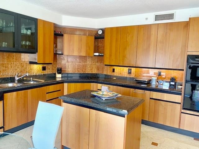 kitchen with light tile patterned floors, a textured ceiling, dark stone countertops, sink, and a center island