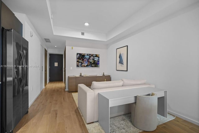 living room featuring light wood-type flooring and a raised ceiling