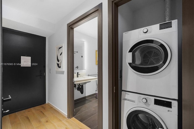 clothes washing area featuring stacked washer / drying machine, light wood finished floors, and baseboards