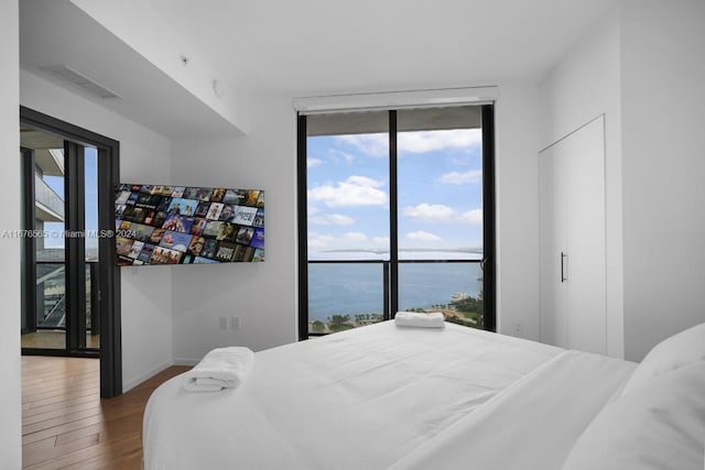 bedroom featuring access to exterior, a water view, dark hardwood / wood-style floors, and floor to ceiling windows