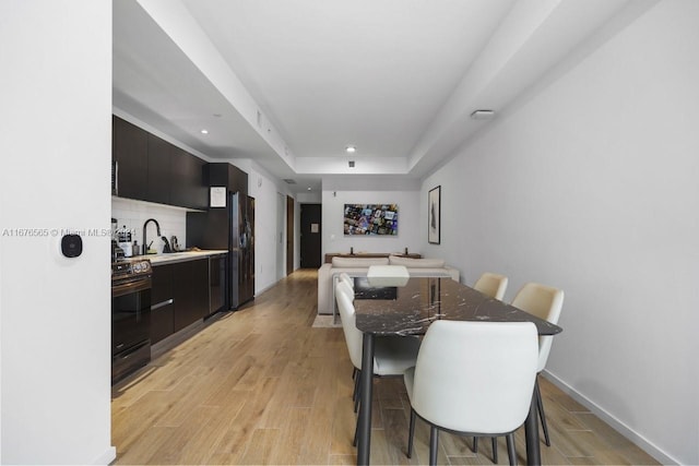 dining room featuring recessed lighting, light wood-style floors, baseboards, and a tray ceiling