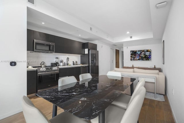 dining room with sink, light hardwood / wood-style floors, and a tray ceiling