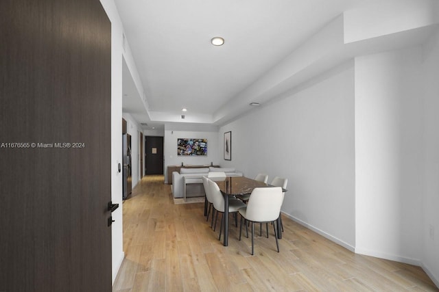 dining room with baseboards, a tray ceiling, light wood-type flooring, and recessed lighting