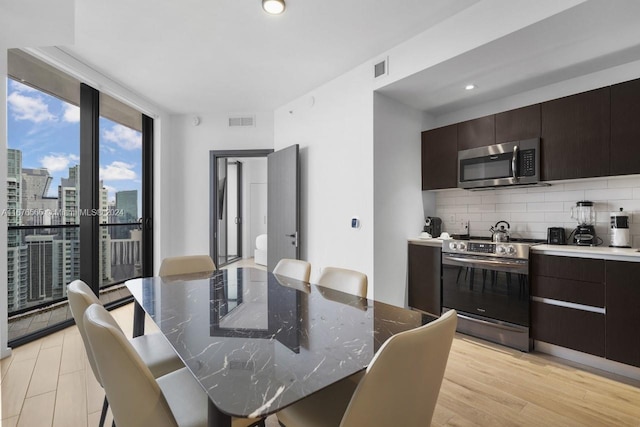 dining space featuring light wood-type flooring, a view of city, visible vents, and a wall of windows