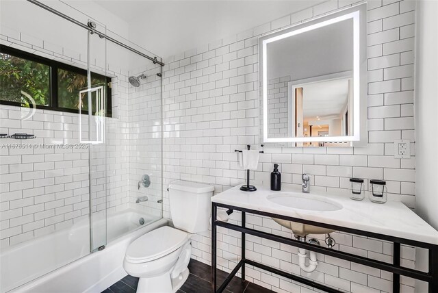 full bathroom featuring tile walls, sink, bath / shower combo with glass door, and toilet