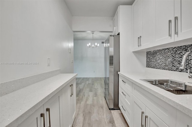 121 NE 204th St Unit 9, Miami Gardens, FL 33179 - kitchen with freestanding refrigerator, white cabinetry, light wood-style floors, backsplash, and a chandelier