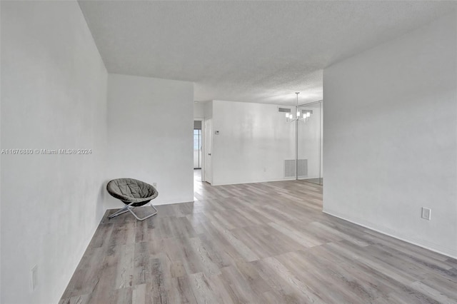 spare room featuring a chandelier, light hardwood / wood-style flooring, and a textured ceiling
