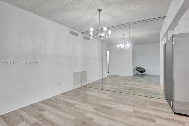 interior space with a chandelier, a textured ceiling, and light wood-type flooring