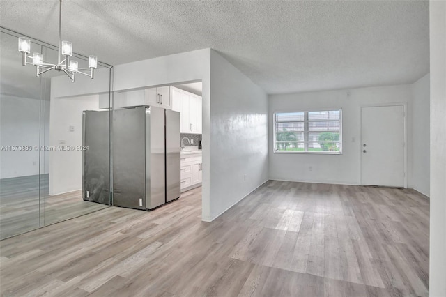 kitchen featuring light wood-type flooring, a textured ceiling, stainless steel fridge, white cabinetry, and decorative light fixtures