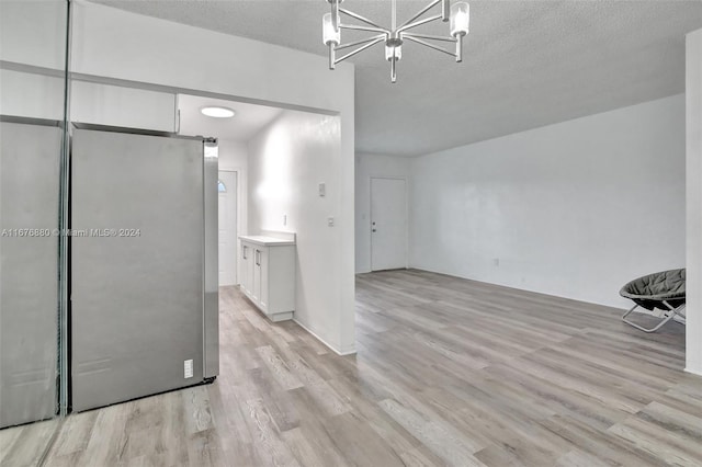 kitchen with stainless steel fridge, a textured ceiling, light wood-type flooring, and white cabinets