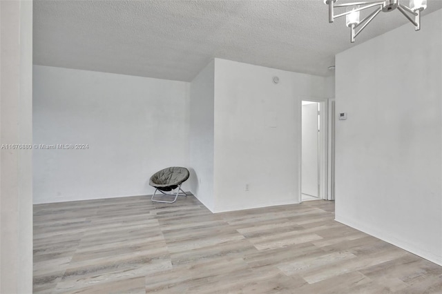 empty room featuring light hardwood / wood-style floors, a textured ceiling, and a chandelier