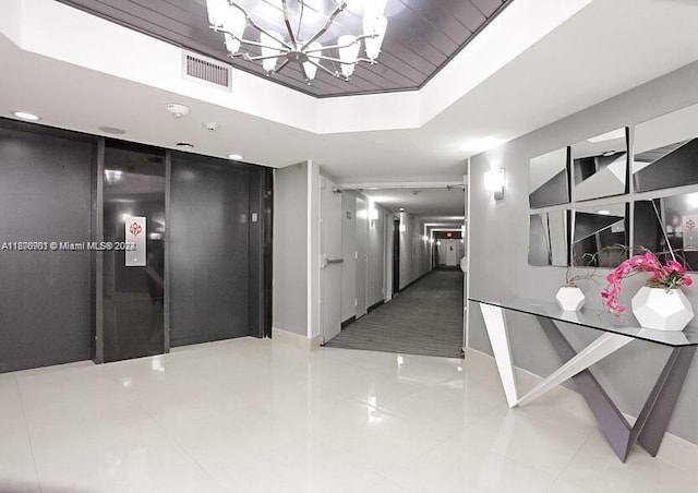 hallway with a chandelier, a tray ceiling, and tile patterned flooring