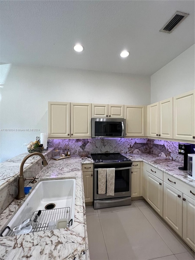 kitchen featuring decorative backsplash, light stone countertops, light tile patterned flooring, sink, and stainless steel appliances