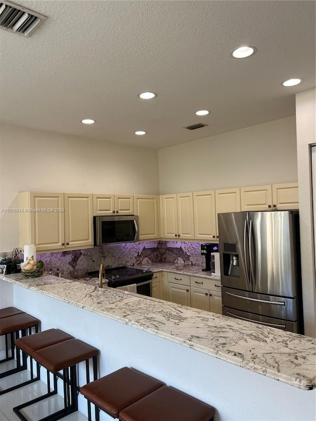 kitchen with appliances with stainless steel finishes, kitchen peninsula, decorative backsplash, and a kitchen breakfast bar