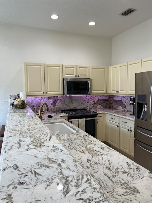 kitchen with tasteful backsplash, appliances with stainless steel finishes, sink, cream cabinetry, and light stone counters