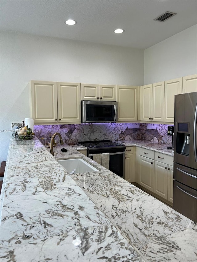 kitchen with cream cabinetry, sink, appliances with stainless steel finishes, light stone counters, and tasteful backsplash