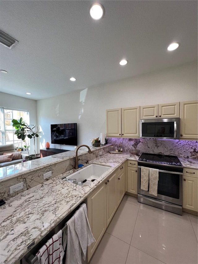 kitchen featuring sink, cream cabinetry, light tile patterned flooring, stainless steel appliances, and light stone counters