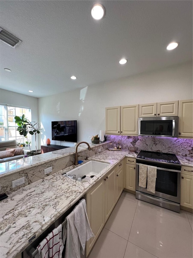 kitchen with cream cabinets, stainless steel appliances, sink, and light tile patterned floors