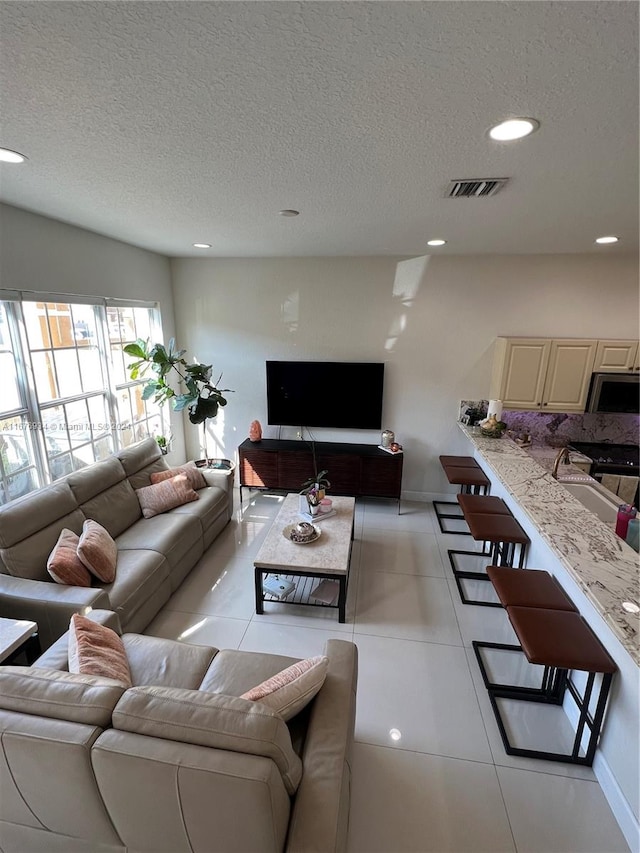 living room featuring sink, a textured ceiling, and light tile patterned floors