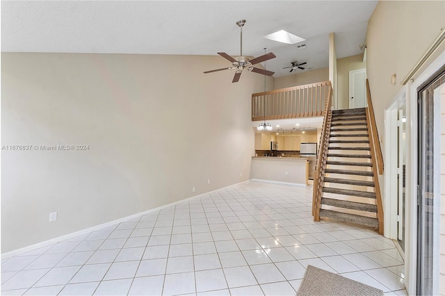 unfurnished living room with ceiling fan, light tile patterned flooring, a towering ceiling, and a skylight