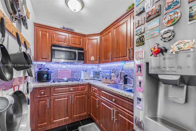 kitchen with dark tile patterned flooring, tasteful backsplash, light stone countertops, appliances with stainless steel finishes, and sink