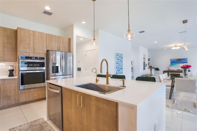 kitchen featuring hanging light fixtures, stainless steel appliances, a center island with sink, sink, and light tile patterned flooring