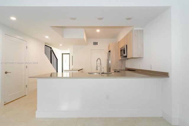 kitchen with light brown cabinetry, appliances with stainless steel finishes, light tile patterned floors, and kitchen peninsula