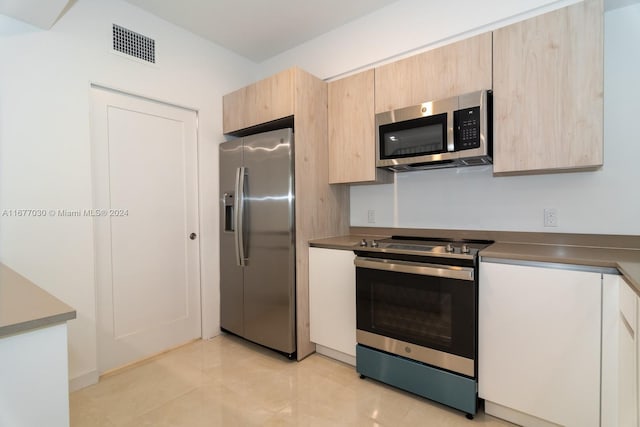 kitchen with light brown cabinetry, appliances with stainless steel finishes, and light tile patterned floors