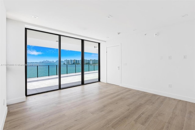 empty room with expansive windows, light wood-style flooring, and baseboards