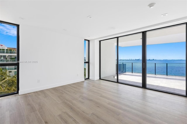 spare room with plenty of natural light, baseboards, a water view, a wall of windows, and light wood-style floors