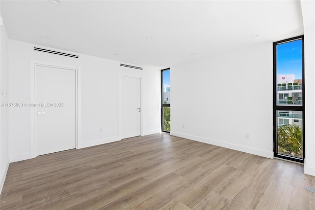 unfurnished room featuring light wood finished floors, baseboards, expansive windows, and visible vents