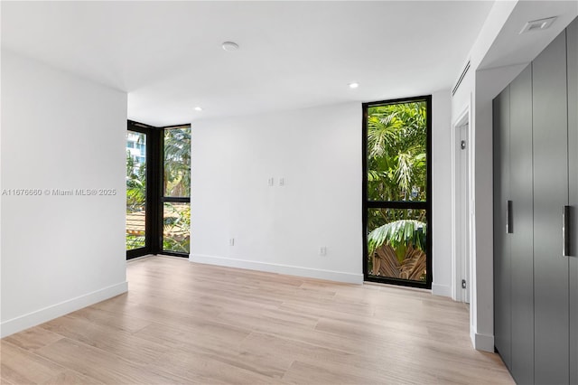 spare room featuring light wood-style floors, recessed lighting, floor to ceiling windows, and baseboards